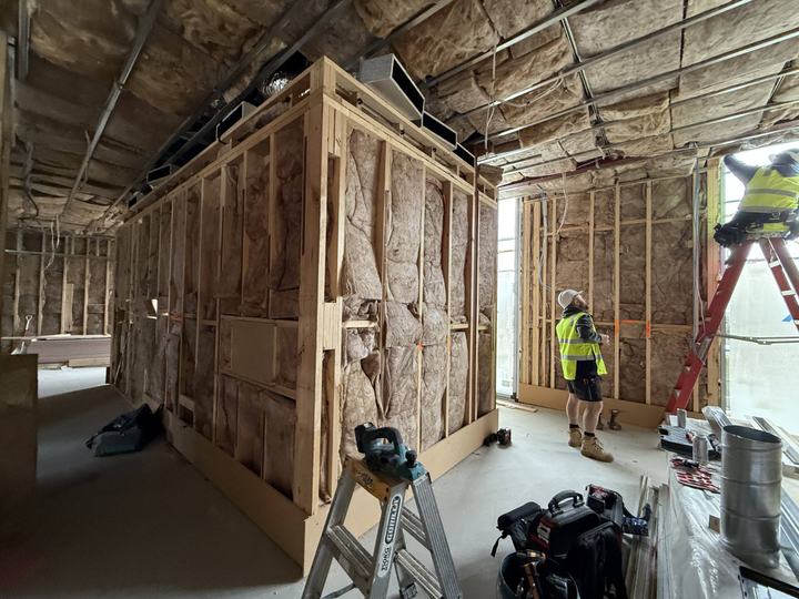 Framed walls with insulation and ducting, with trades working on the services.