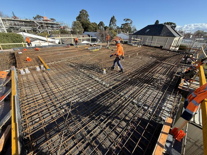 Workers in high-vis walking on steel reinforcement laid out for a concrete slab.